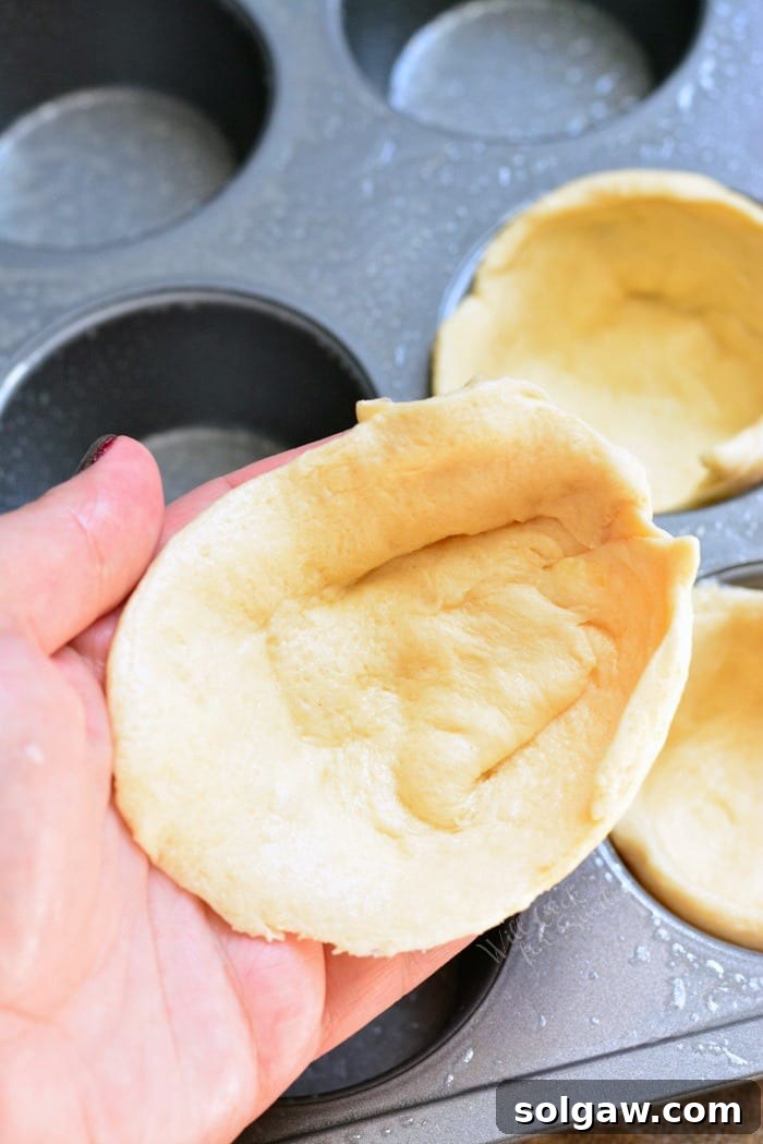 Crescent dough cups placed in a muffin tin, ready for filling