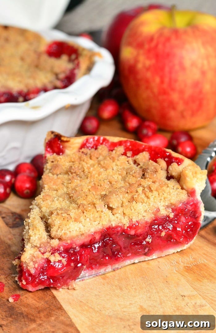 Delicious Apple Cranberry Pie on a rustic wood cutting board, surrounded by fresh cranberries and apples, ready to be served.