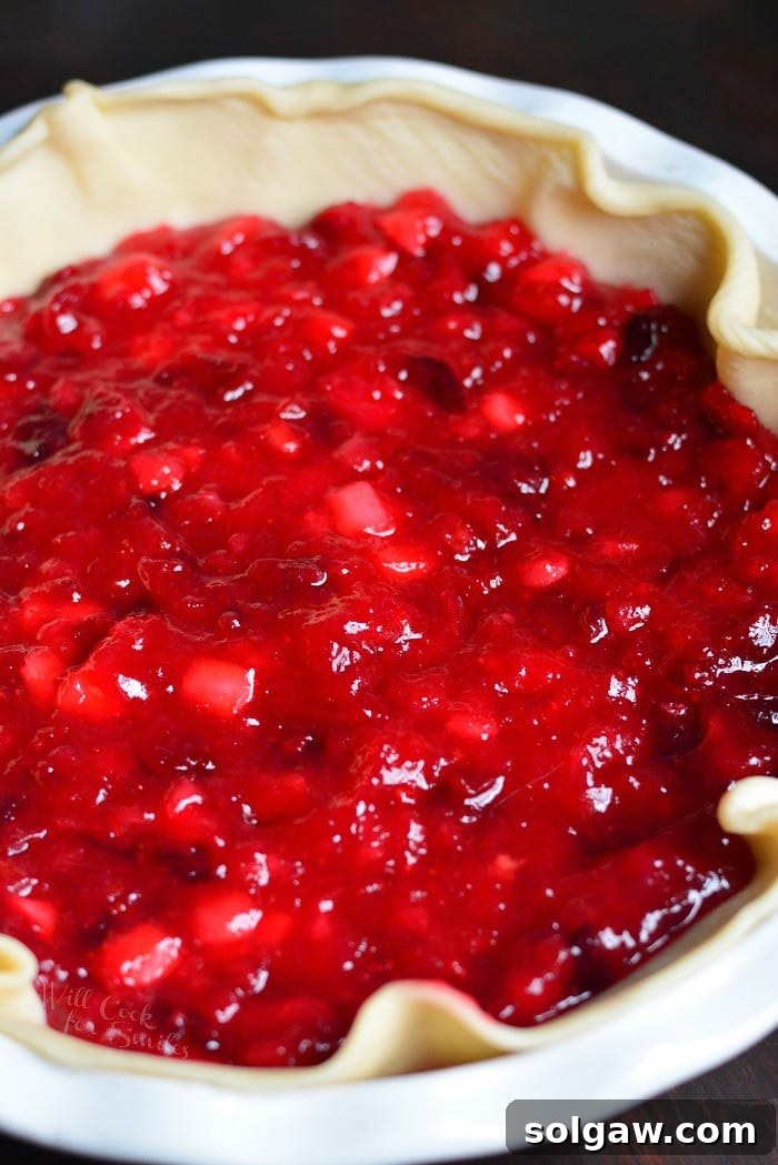 Uncooked Apple Cranberry Pie in a pie pan with prepared streusel topping on the side, ready for baking.
