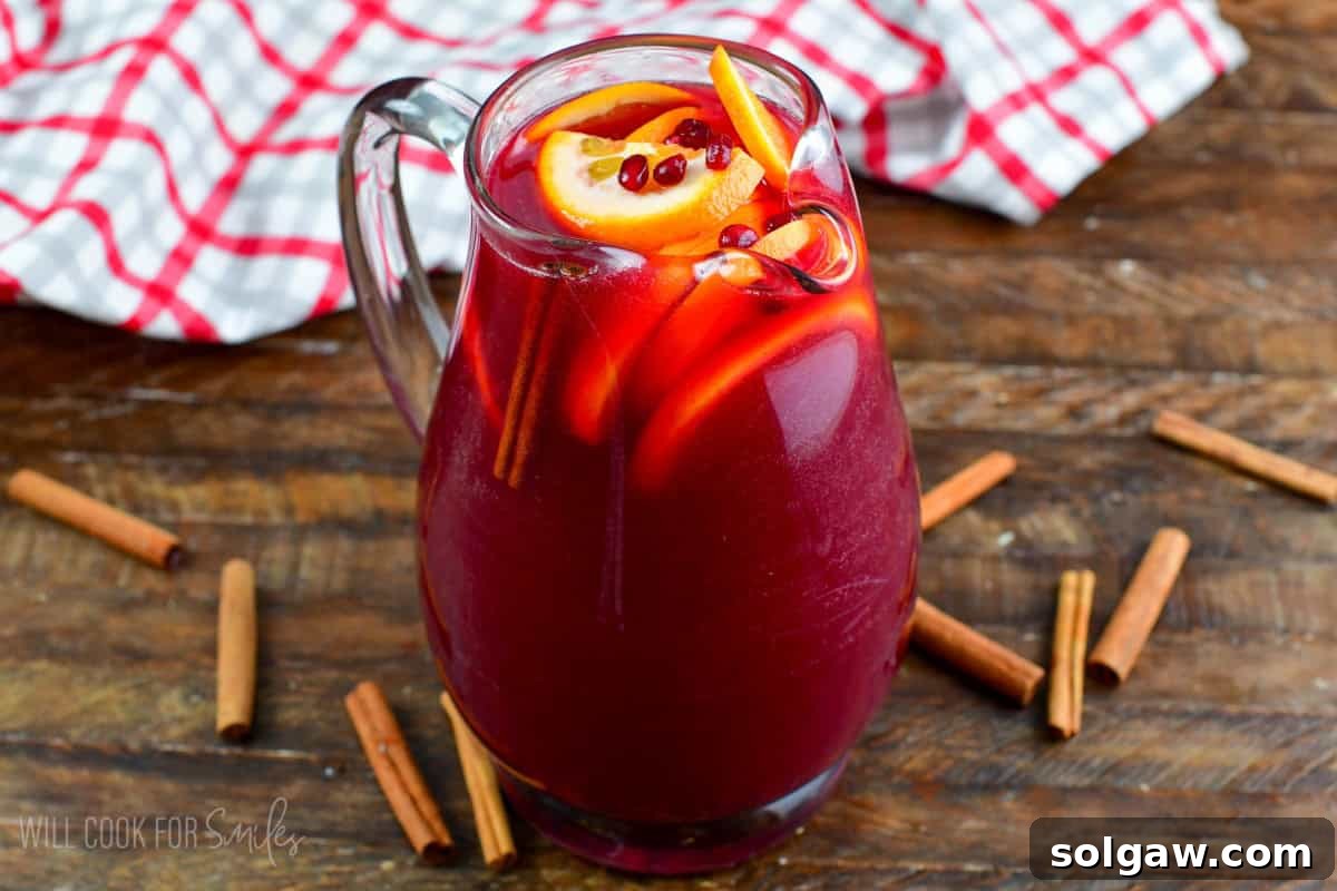 Christmas punch served in a pitcher, garnished with vibrant orange slices, glistening pomegranate seeds, and fragrant cinnamon sticks, ready for holiday serving.