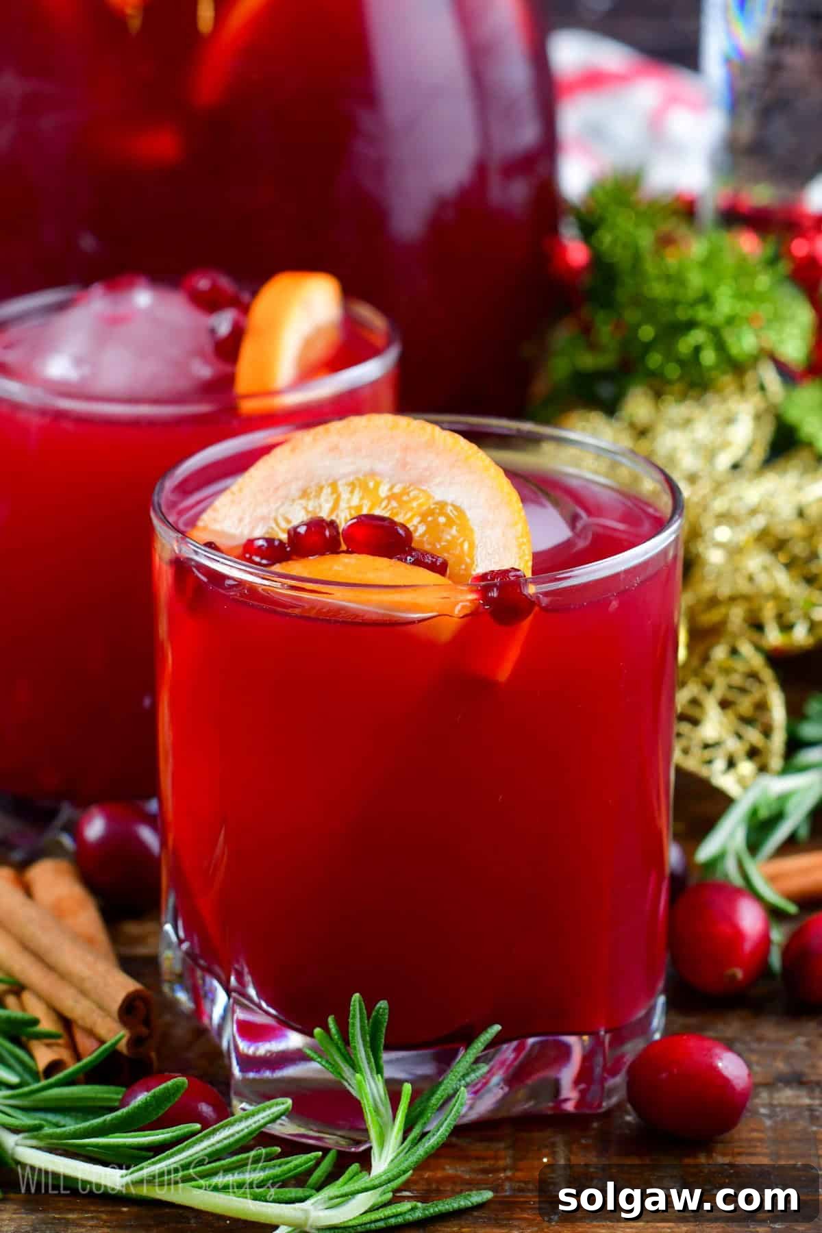 Christmas punch in a glass with another behind with rosemary, cranberries and cinnamon sticks around.