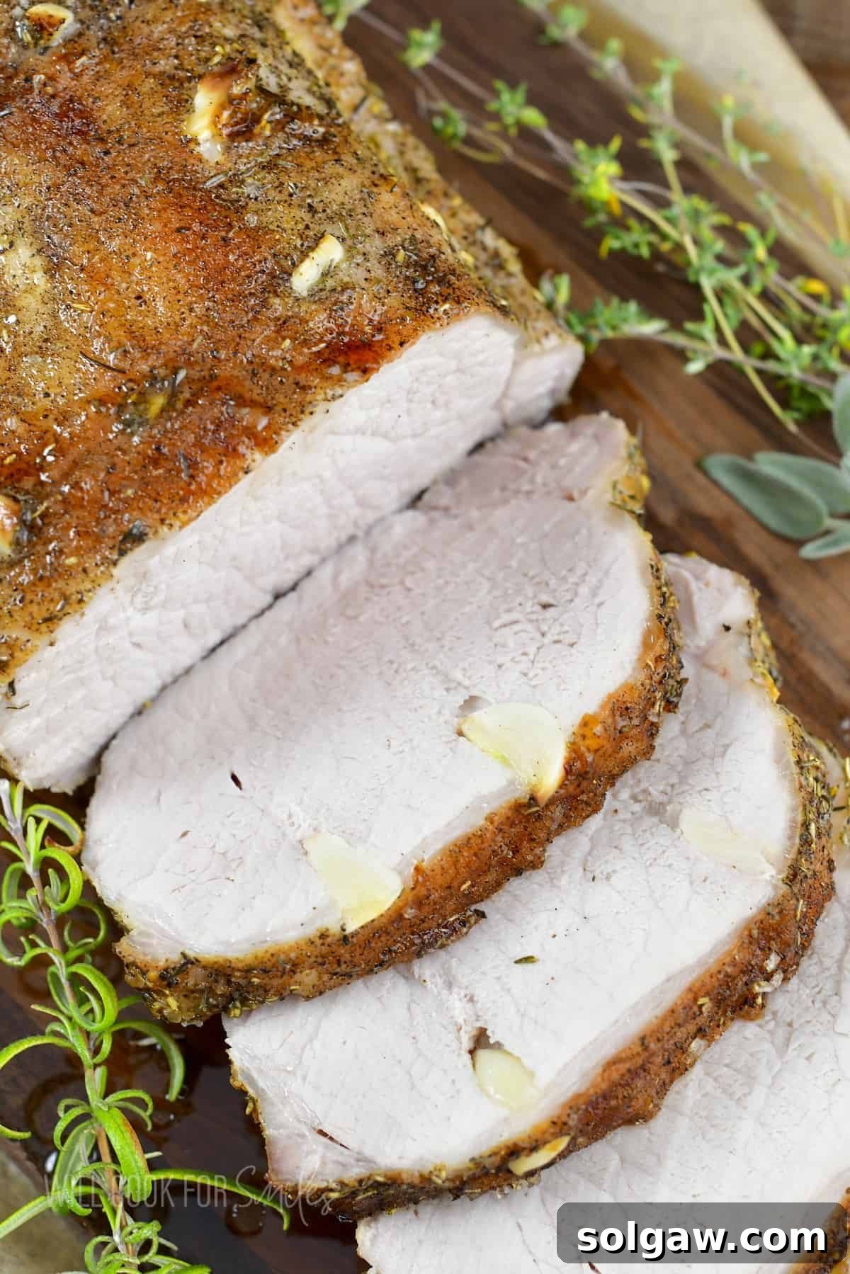 Aromatic Garlic Pork Loin 11 closeup of sliced garlic pork loin on the board with herbs.