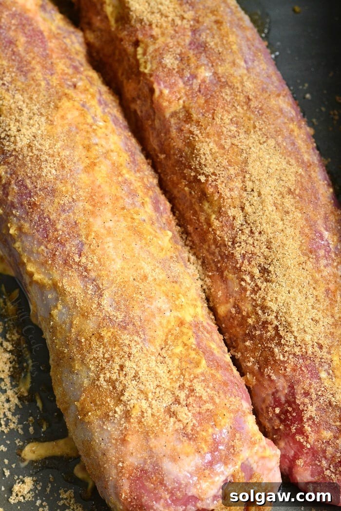 uncooked pork tenderloins side by site in a roasting dish with seasoning over it.