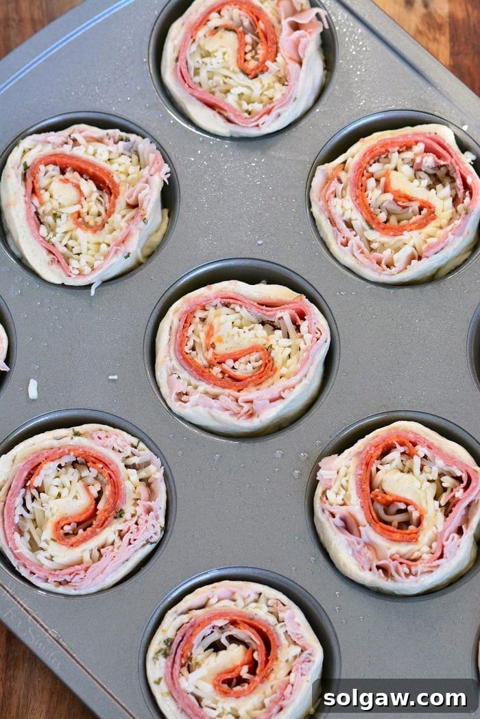 Uncooked Italian Sub Pinwheels arranged in a muffin pan, ready to be baked.
