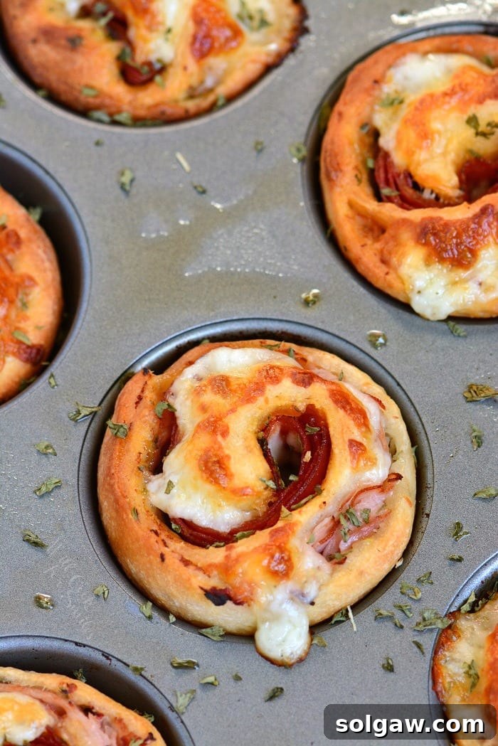 Freshly baked Italian Sub Pinwheels in a muffin pan, golden brown and bubbly.