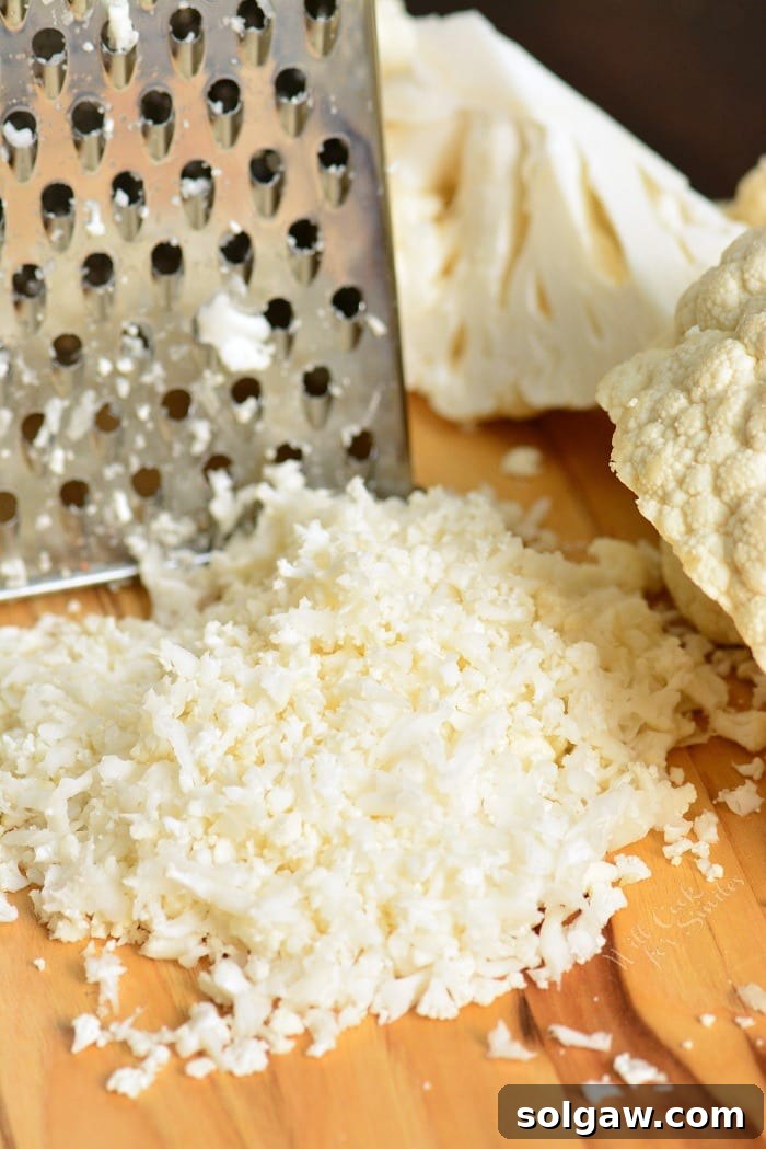 Cauliflower being shredded with grater onto a cutting board  