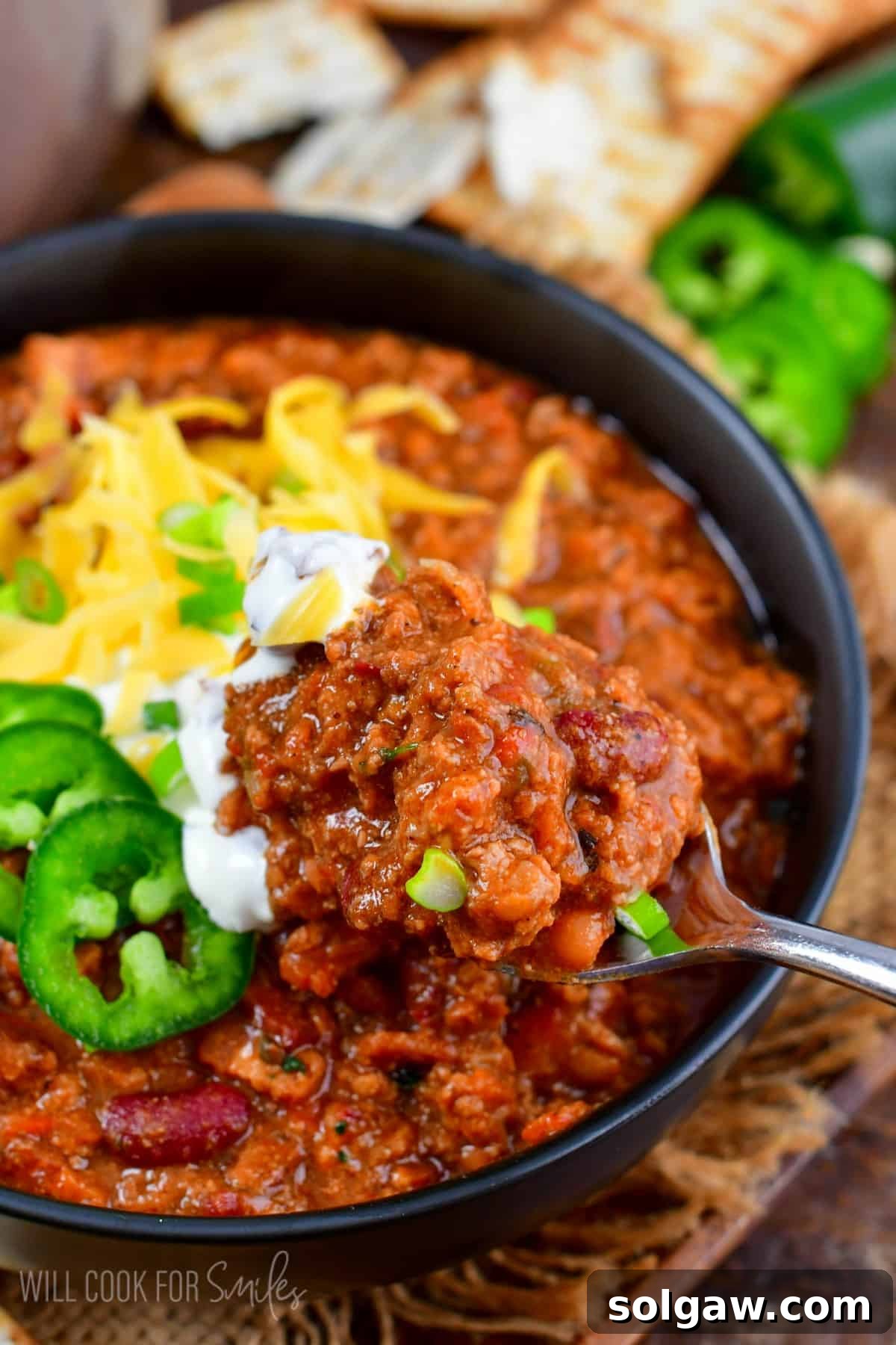 A hearty bowl of homemade beef chili, rich with bacon, ground beef, vegetables, and beans, served with a spoon. Perfect comfort food for any occasion.