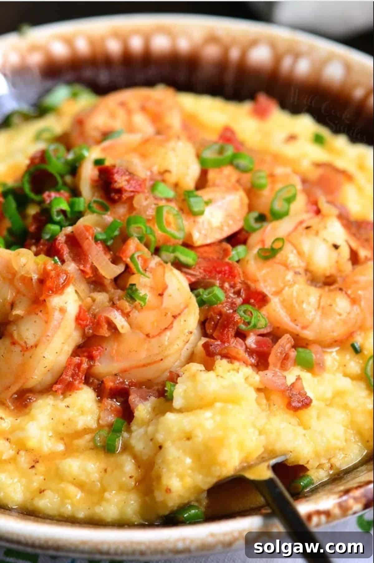 Southern Comfort Shrimp and Grits 7 A serving spoon scooping out cheesy grits from a bowl topped with shrimp.