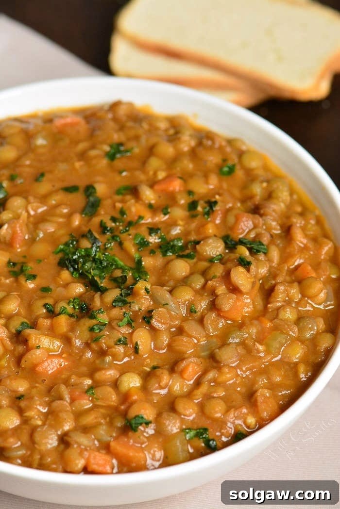 A pristine white bowl overflowing with steaming lentil soup, exquisitely garnished with a flourish of fresh, vibrant greens, highlighting its wholesome appeal.