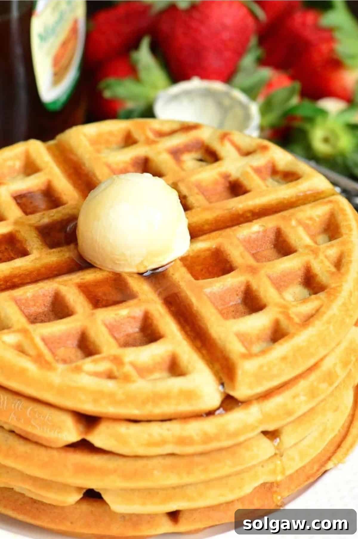 Golden brown buttermilk waffles stacked on a plate with melting butter and maple syrup drizzled over them.