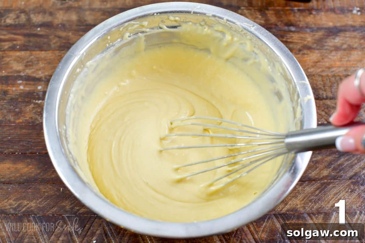 A light-colored waffle batter being vigorously whisked in a gleaming metal mixing bowl.