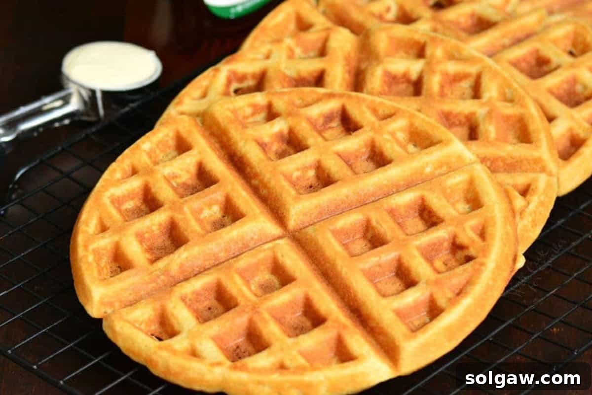 Three golden brown waffles neatly lined up on a metal wire rack, cooling down after being cooked.
