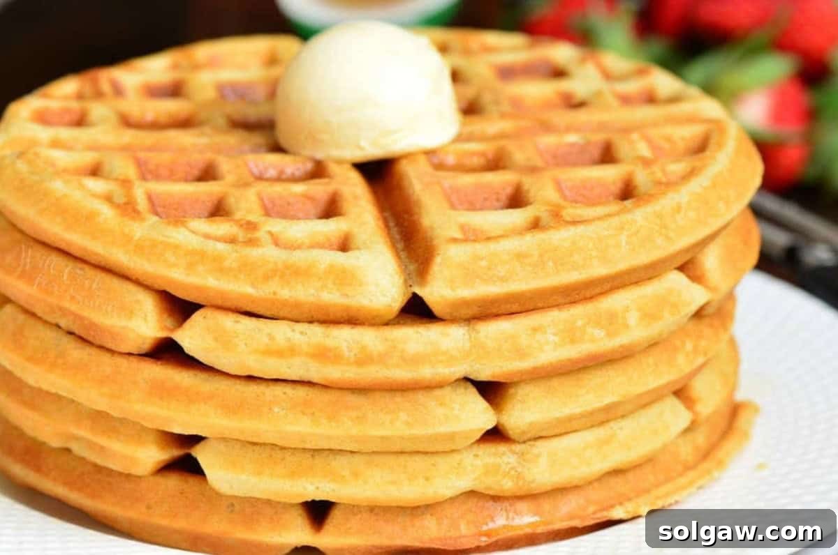 A mouth-watering stack of fluffy buttermilk waffles on a white plate, topped with a generous dollop of butter.