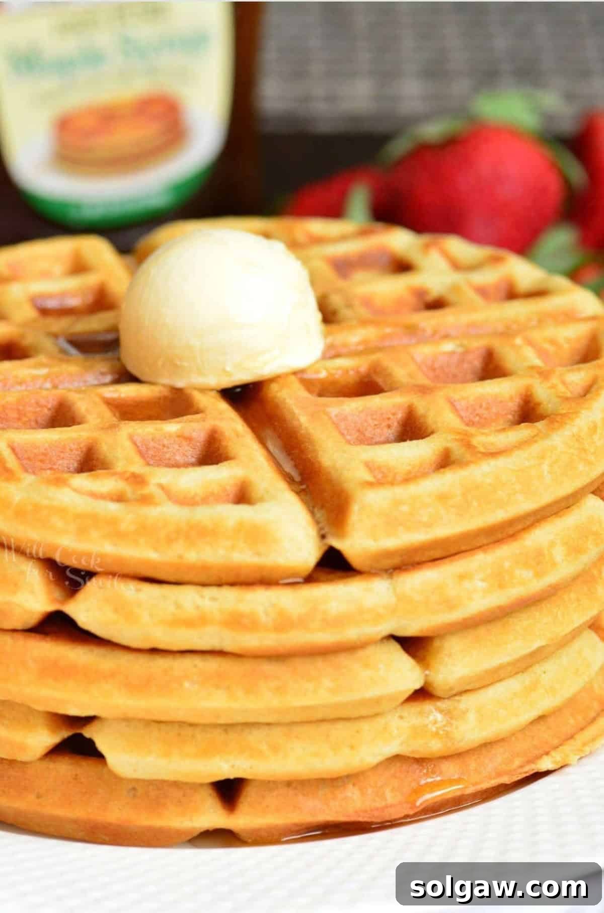 Waffles stacked up on a plate with a dollop of butter on top.