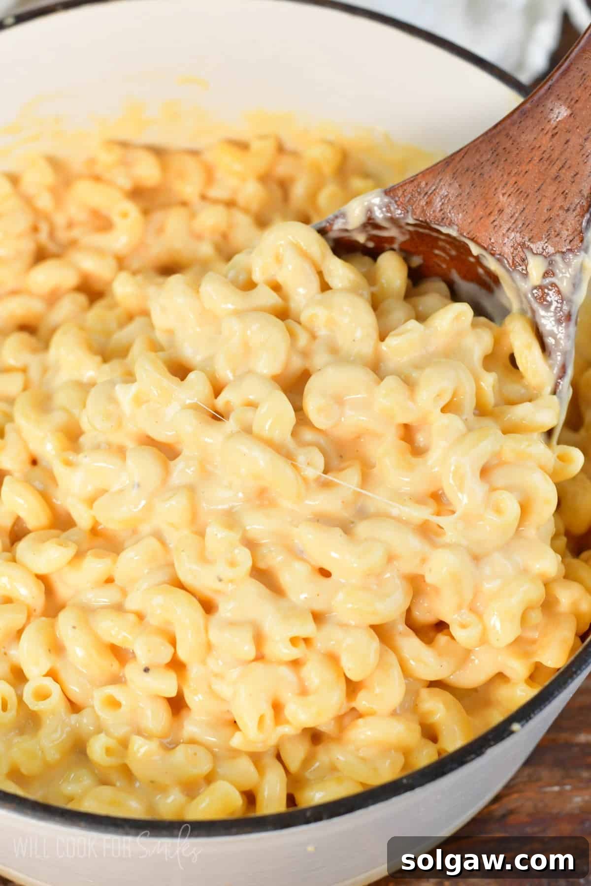 A large ladle scooping a generous portion of rich, creamy, and wonderfully cheesy mac and cheese from a pot, steam gently rising.