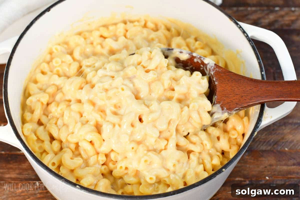 A large white pot filled with homemade mac and cheese, with a wooden ladle scooping out a generous portion.