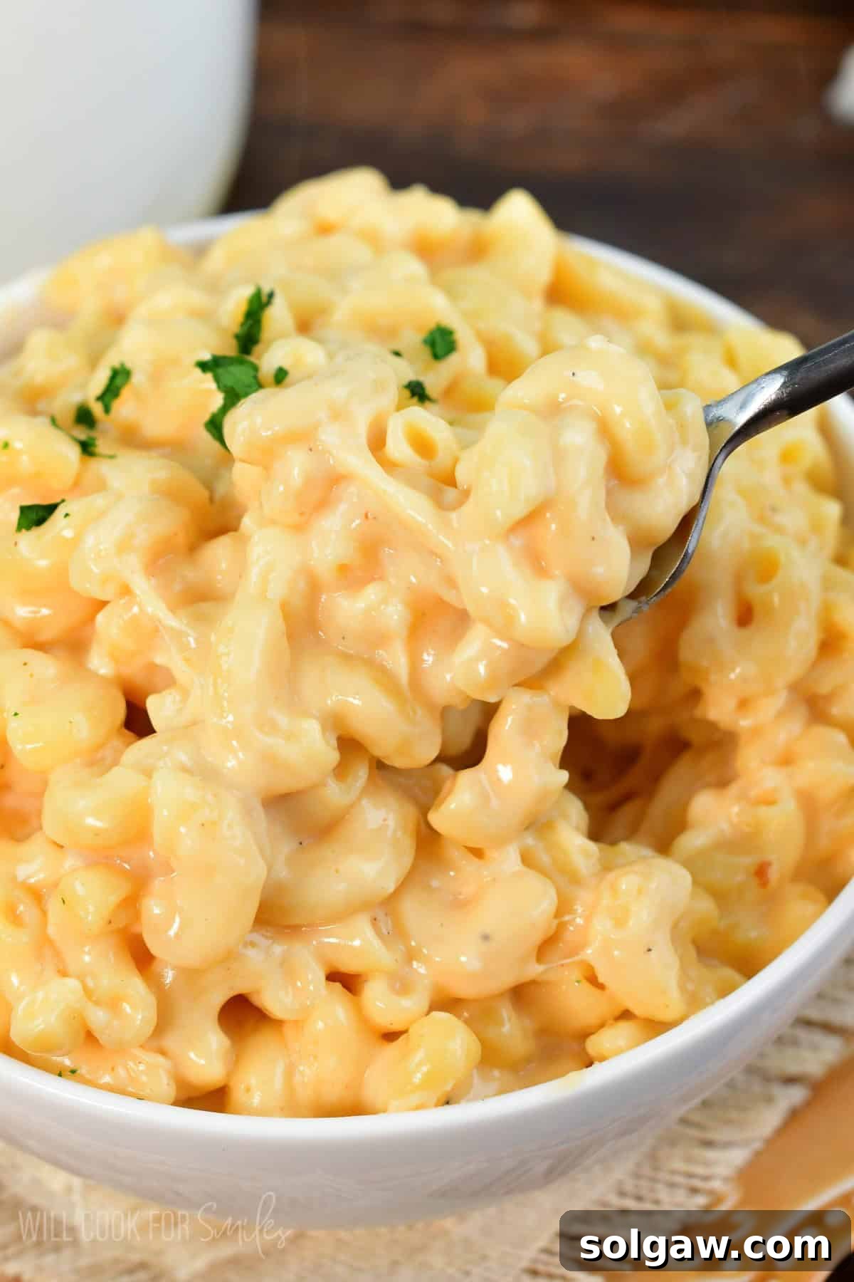 A fork scooping a generous bite of creamy, cheesy mac and cheese from a white bowl, showing the gooey texture.