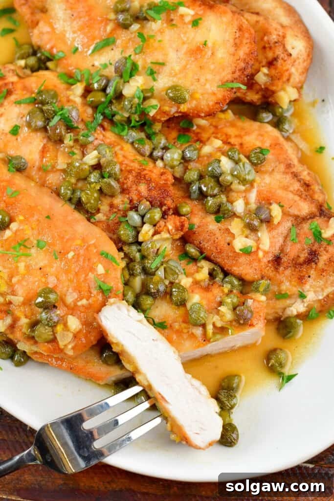 Closeup of perfectly sliced chicken piccata on a plate, showing the tender white meat and glistening lemon-caper sauce.