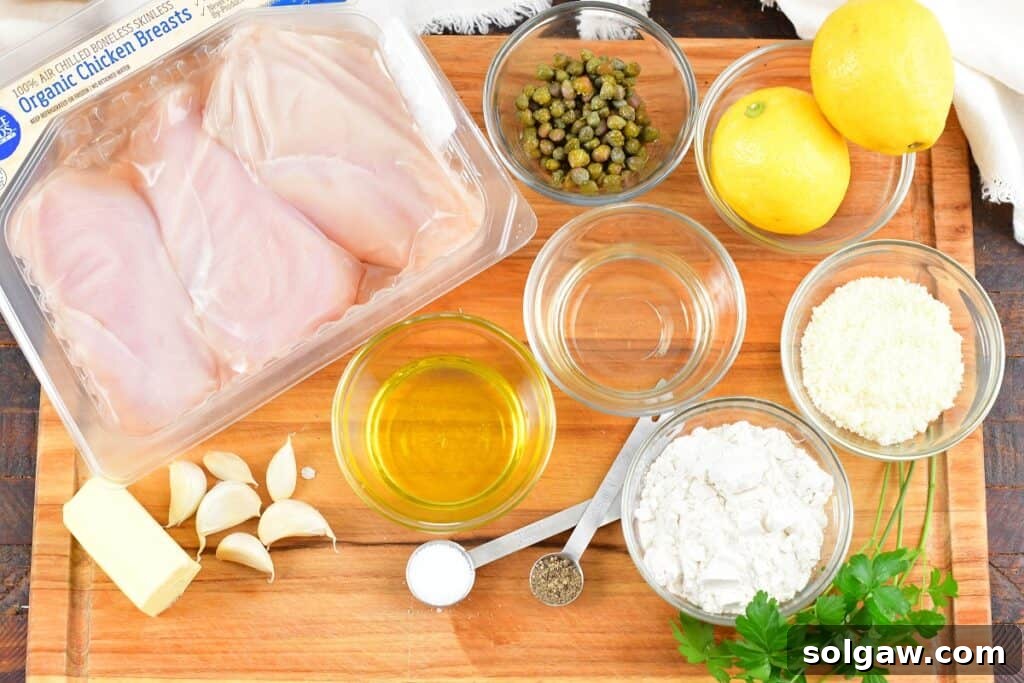 A selection of fresh ingredients laid out on a kitchen counter, including chicken breasts, lemons, garlic, capers, butter, olive oil, and parsley, ready for making Chicken Piccata.