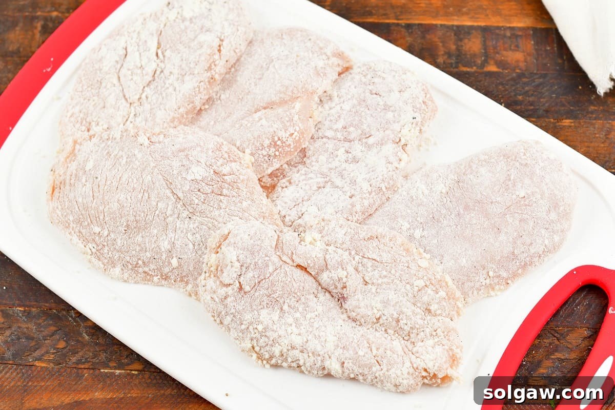 Several dredged chicken cutlets neatly arranged on a cutting board, ready for searing.
