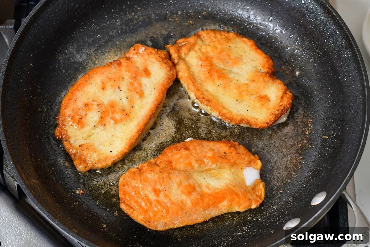 Seared dredged chicken cutlets resting in a pan, having achieved a beautiful golden color on both sides.