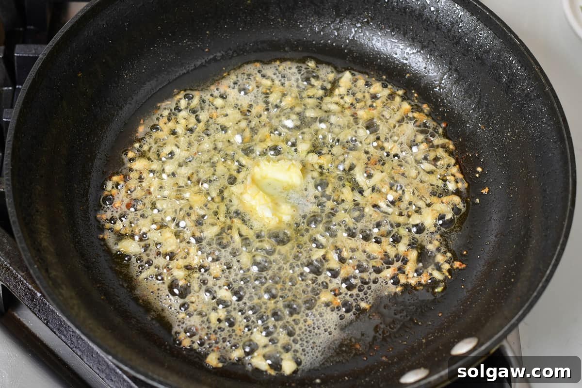 Minced garlic gently sautéing in melted butter and olive oil in a pan, releasing its fragrant aroma.