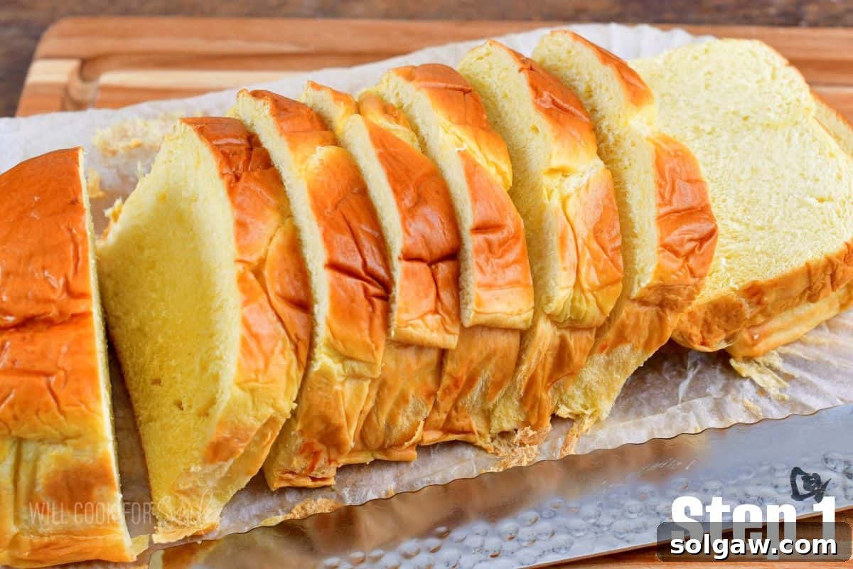 A fresh loaf of Brioche bread, perfectly sliced for French Toast, resting on a wooden cutting board beside a knife.
