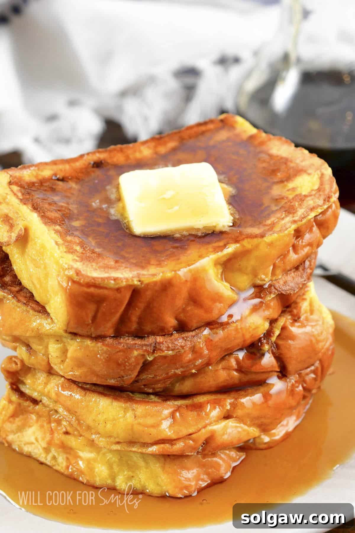 A delectable stack of golden French Toast slices, generously topped with a pat of melting butter and a drizzle of rich maple syrup, served on a light-colored plate.