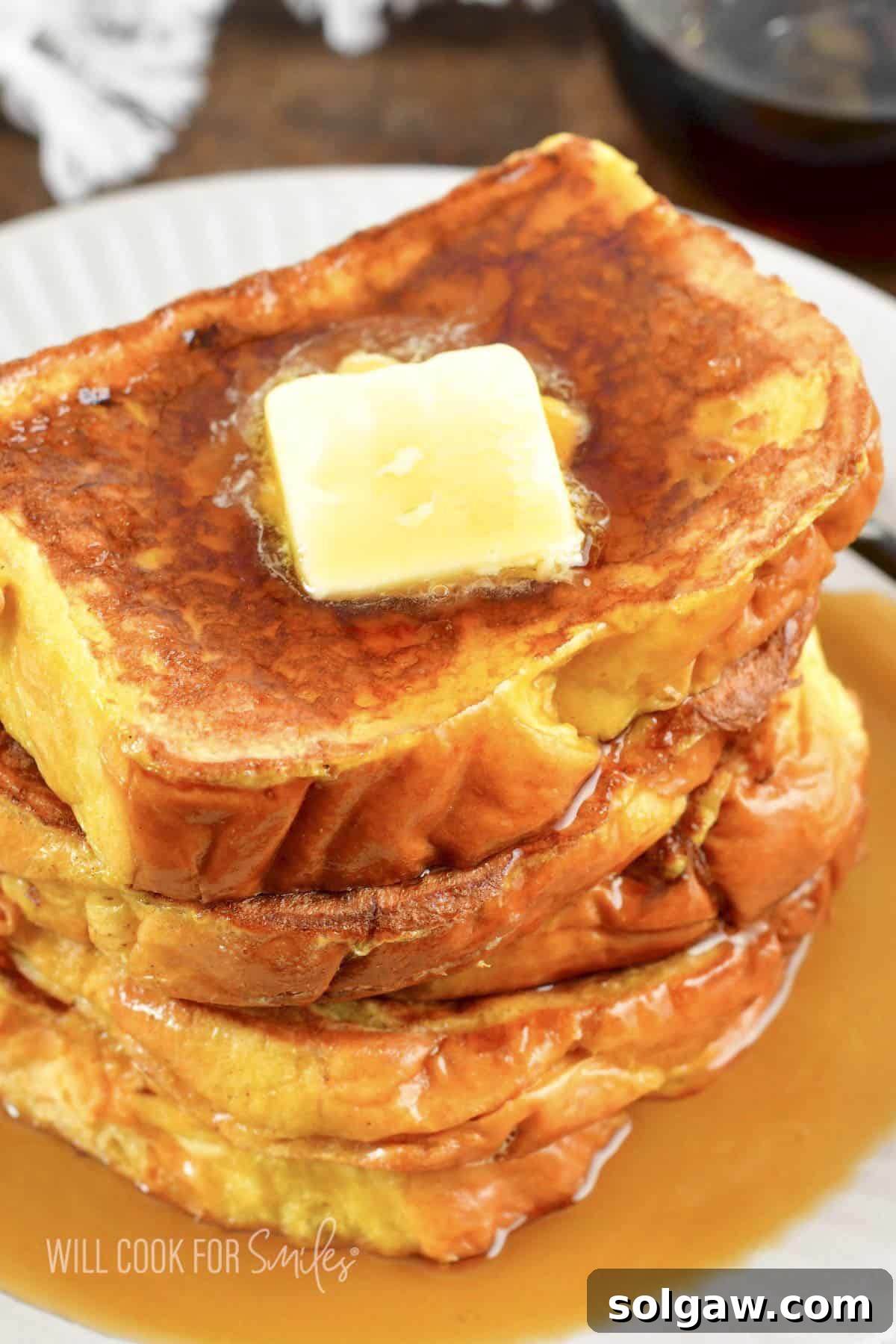Several slices of French Toast stacked with butter and syrup on top.