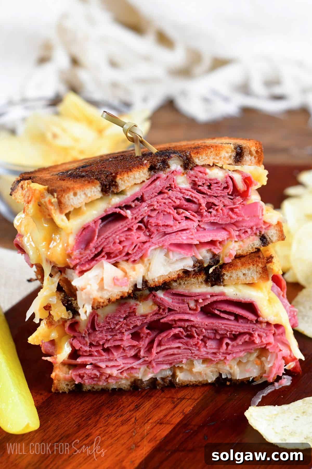 A perfectly halved Reuben sandwich, showing layers of corned beef, Swiss cheese, sauerkraut, and dressing, resting on a wooden cutting board.