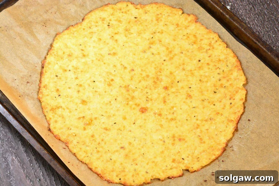 Cauliflower Pizza Crust cooked on parchment paper on a baking sheet sitting on a wood cutting board