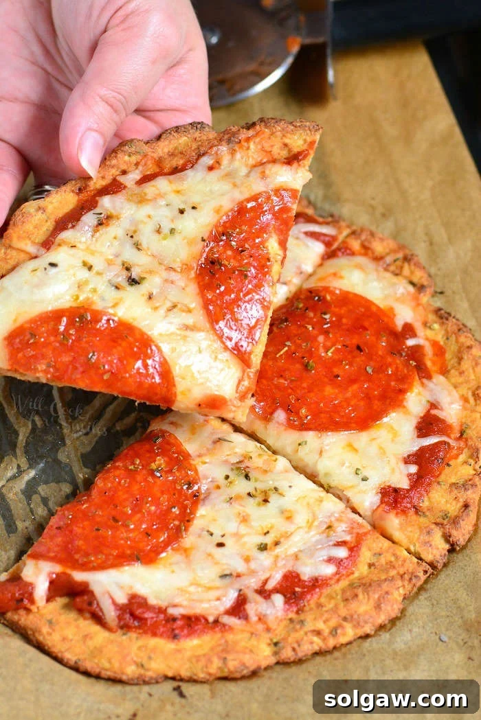 Cauliflower Pizza Crust pepperoni pizza on parchment paper with me holding a slice