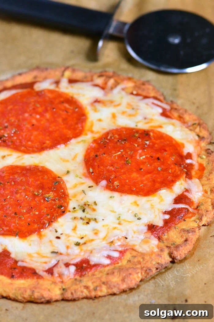 Cauliflower Pizza Crust pepperoni pizza un sliced on parchment paper with pizza cutter