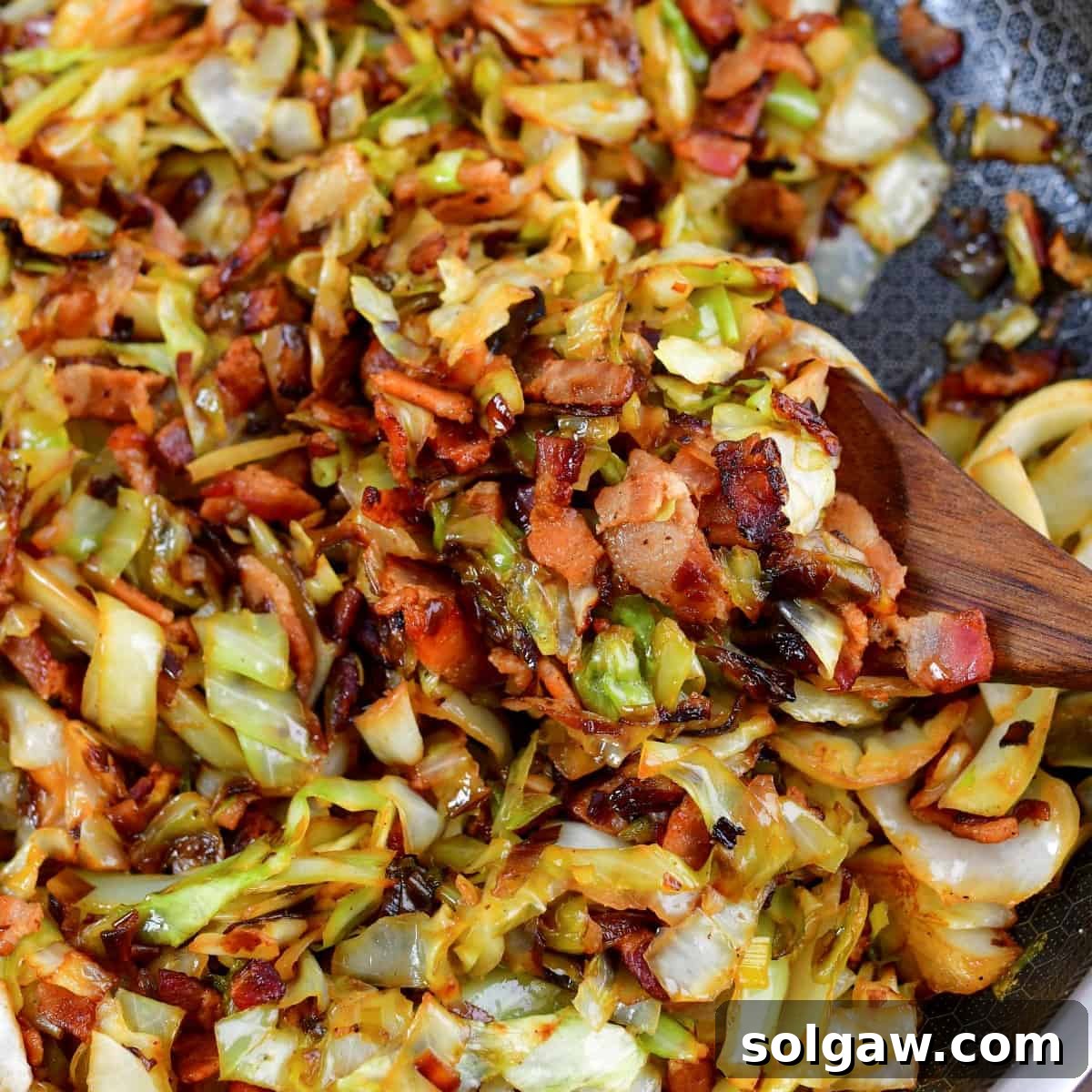 Closeup of a scoop of fried cabbage with bacon, showcasing the crispy texture and golden color.