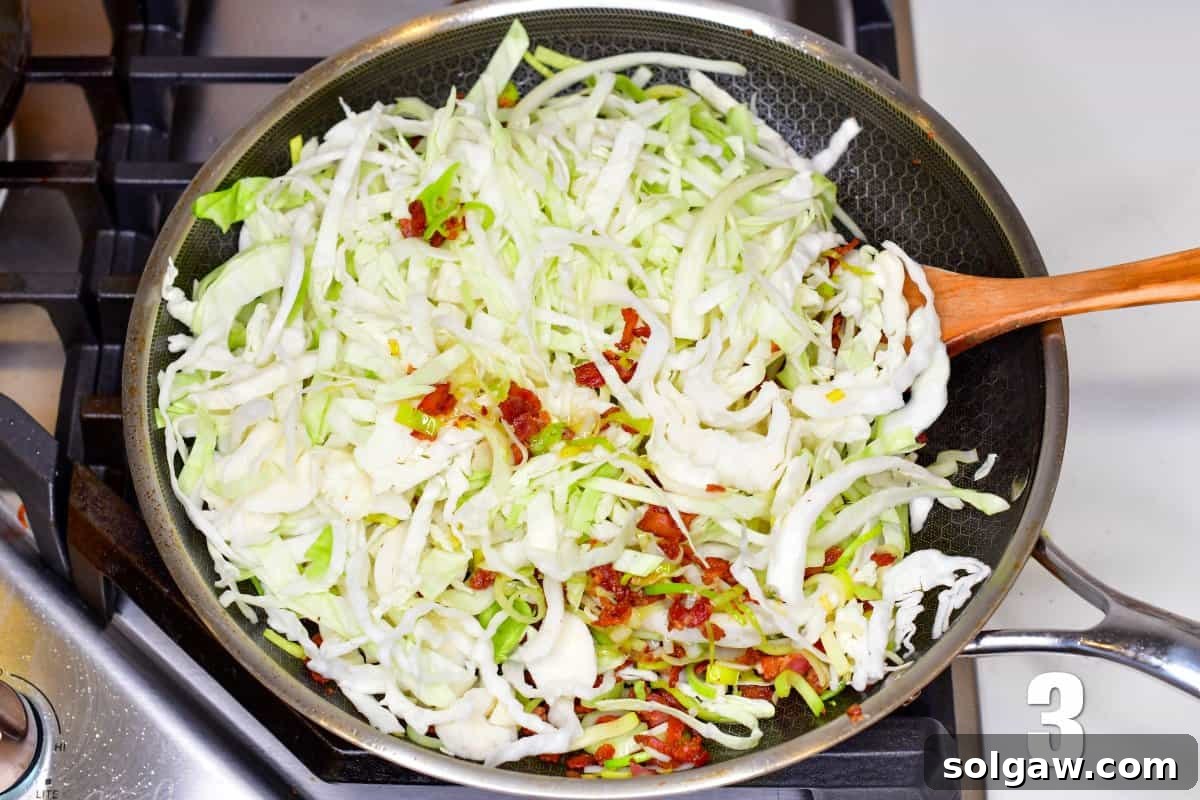 Freshly sliced green cabbage being added to a pan with sautéed bacon and leeks, ready to be stirred.