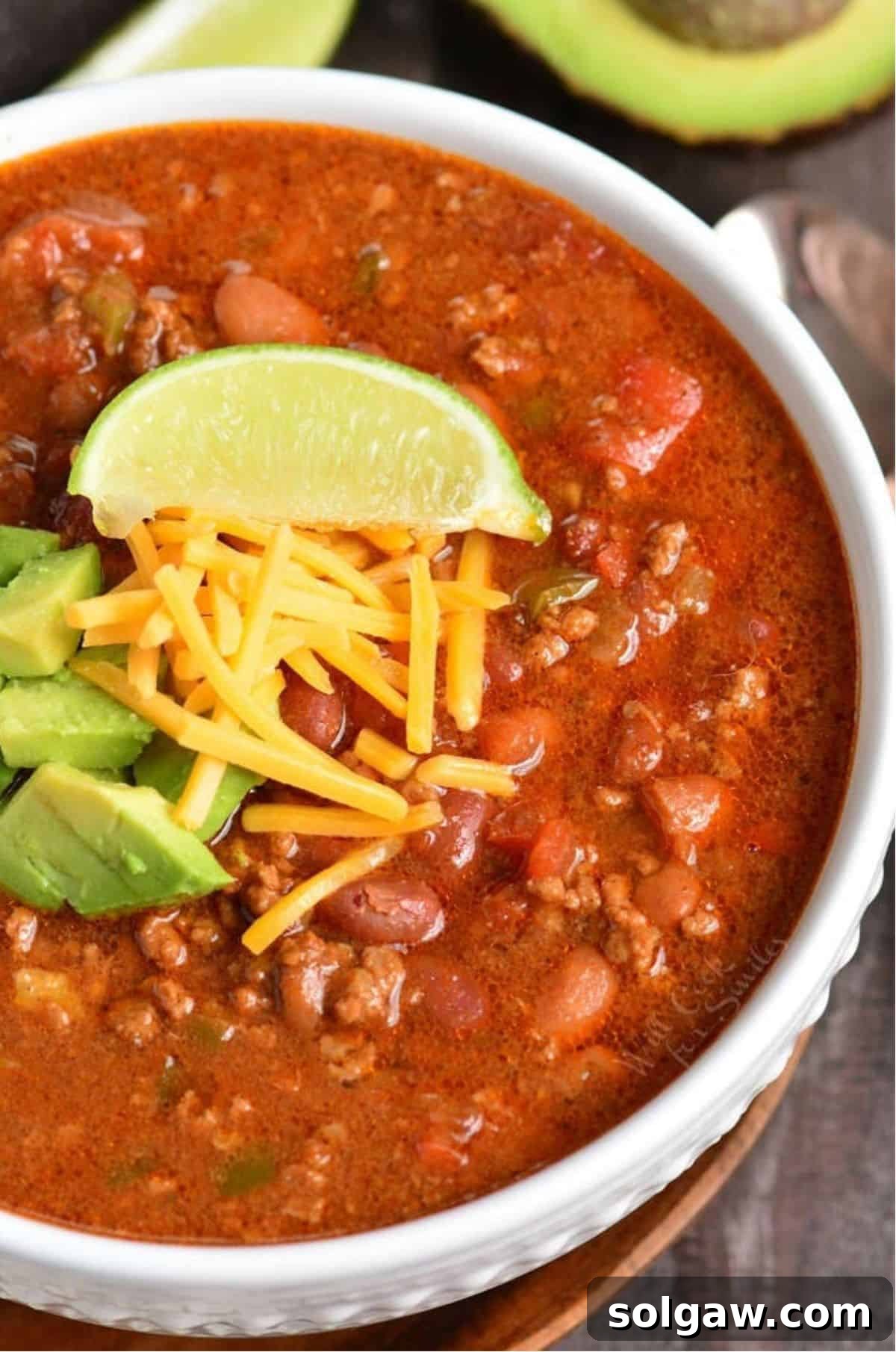 A hearty bowl of Instant Pot Chili garnished with shredded cheese, diced avocado, and a fresh lime wedge.