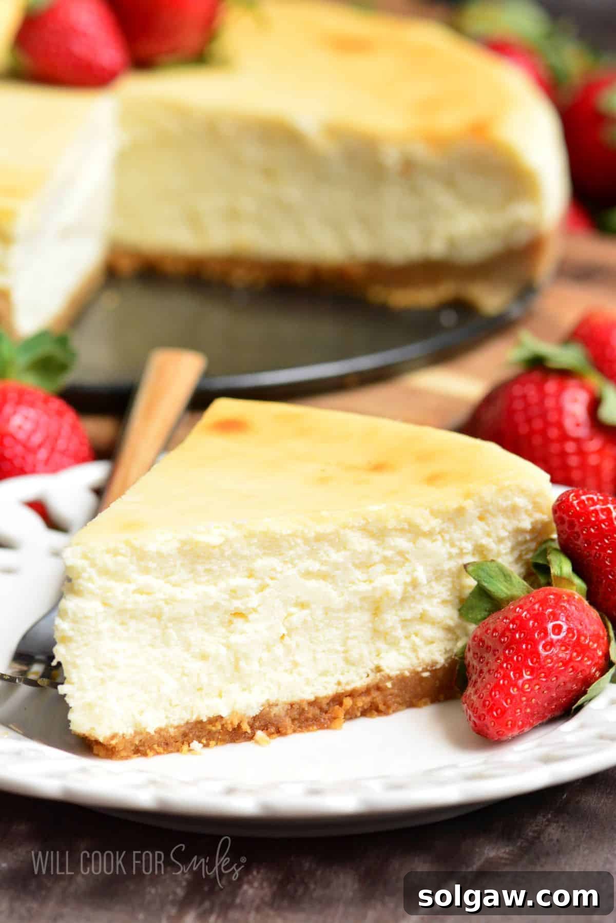 slice of classic New York cheesecake on a plate with fresh strawberries and a fork, highlighting its creamy texture.