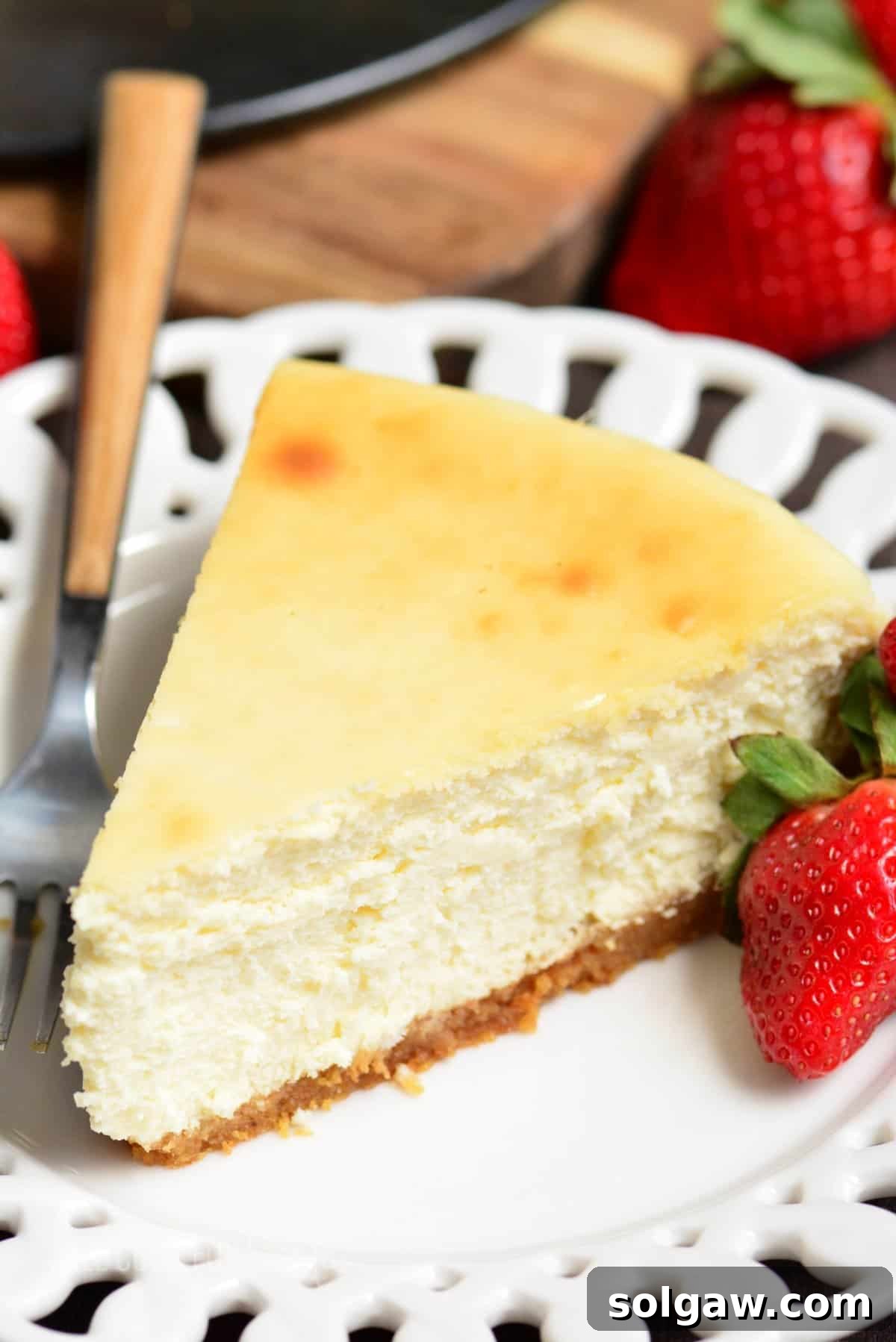slice of classic cheesecake on a white plate with a fork and a strawberry.