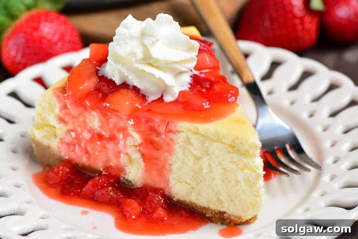 A delectable slice of classic cheesecake topped with vibrant strawberry topping and a dollop of whipped cream on a white plate, ready to be enjoyed.