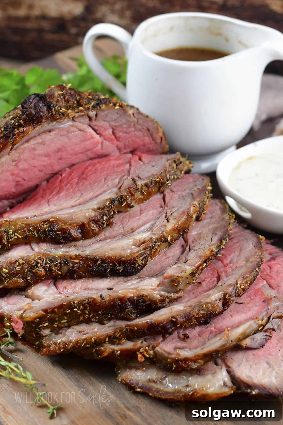 side view of sliced prime rib with bowls of au jus and horseradish sauce.