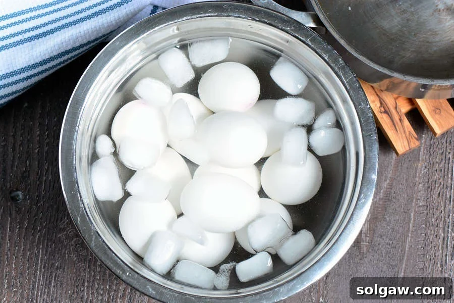 Hard boiled eggs rapidly cooling in an ice bath within a metal bowl to stop the cooking process.