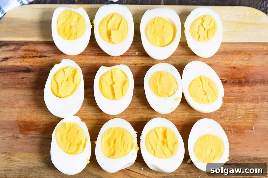 Perfectly cooked hard-boiled eggs, halved lengthwise and lined up neatly on a wooden cutting board.