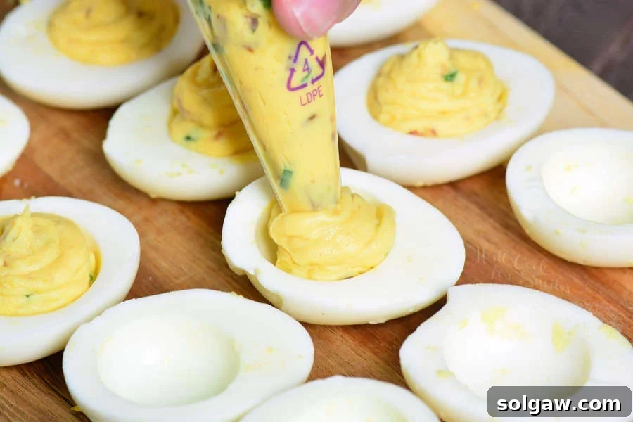A piping bag precisely filling a halved hard-boiled egg white with smooth, creamy deviled egg mixture.