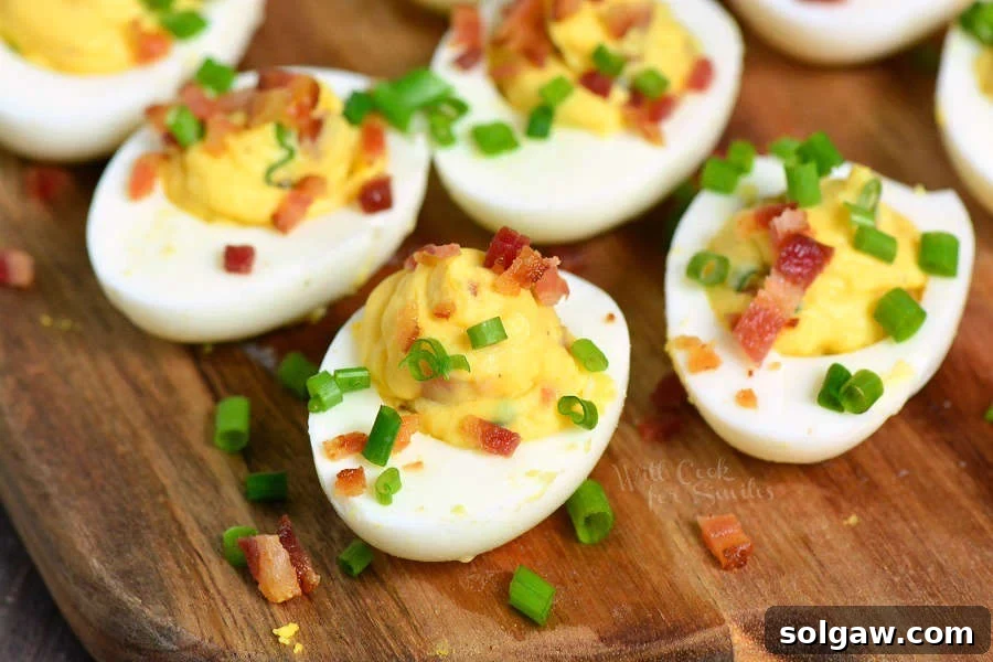 A few creamy deviled eggs topped with crispy bacon and fresh chives, arranged on a rustic wooden cutting board.