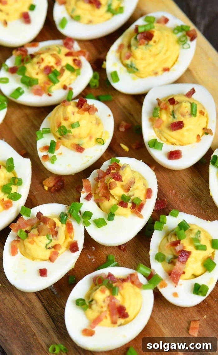 Several creamy and smooth bacon deviled eggs with fresh chives, artfully arranged on a rustic wooden plate.