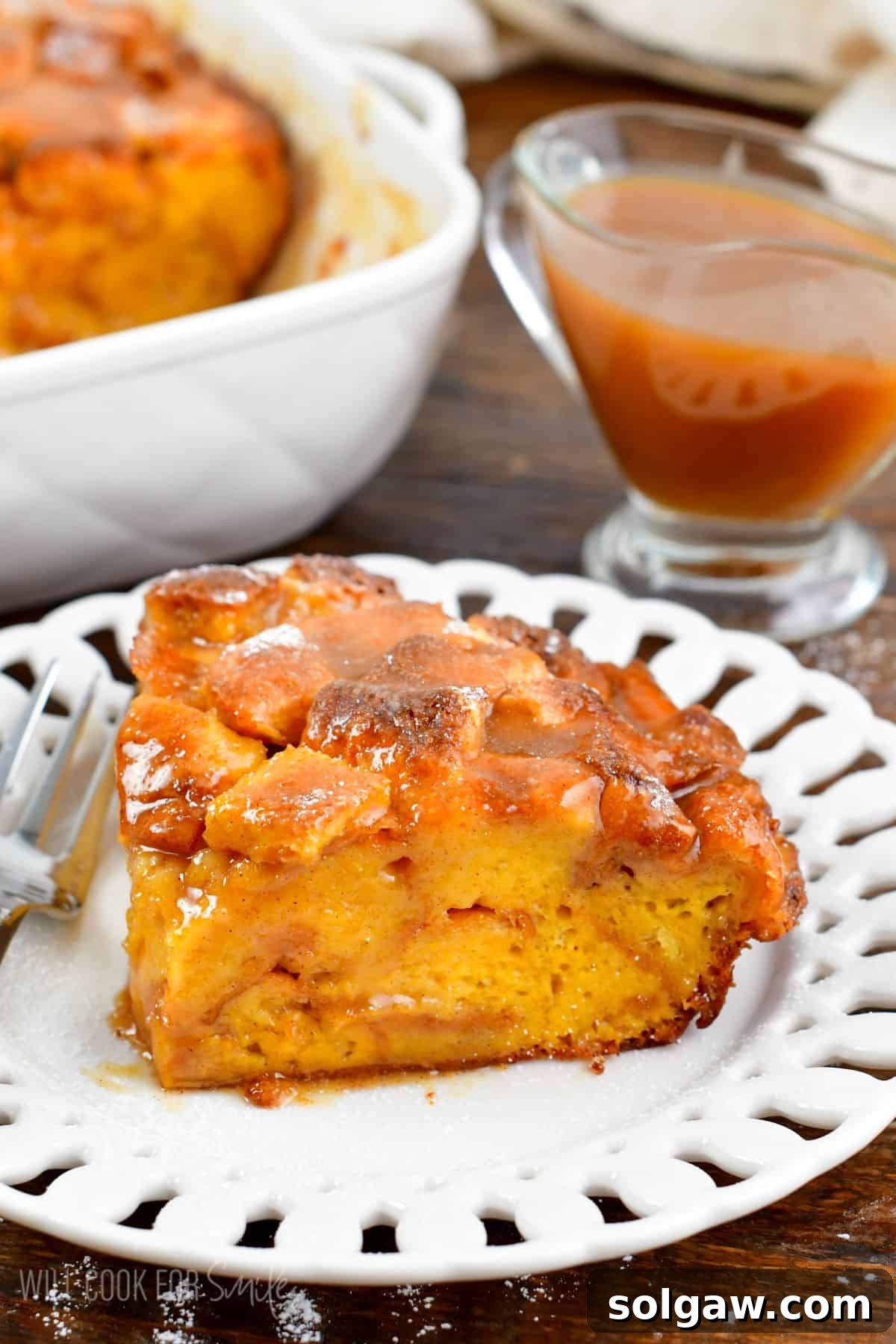 A perfect slice of French toast casserole on a pristine white plate, accompanied by a fork and a small saucer of extra sweet syrup, highlighting its appetizing appeal.