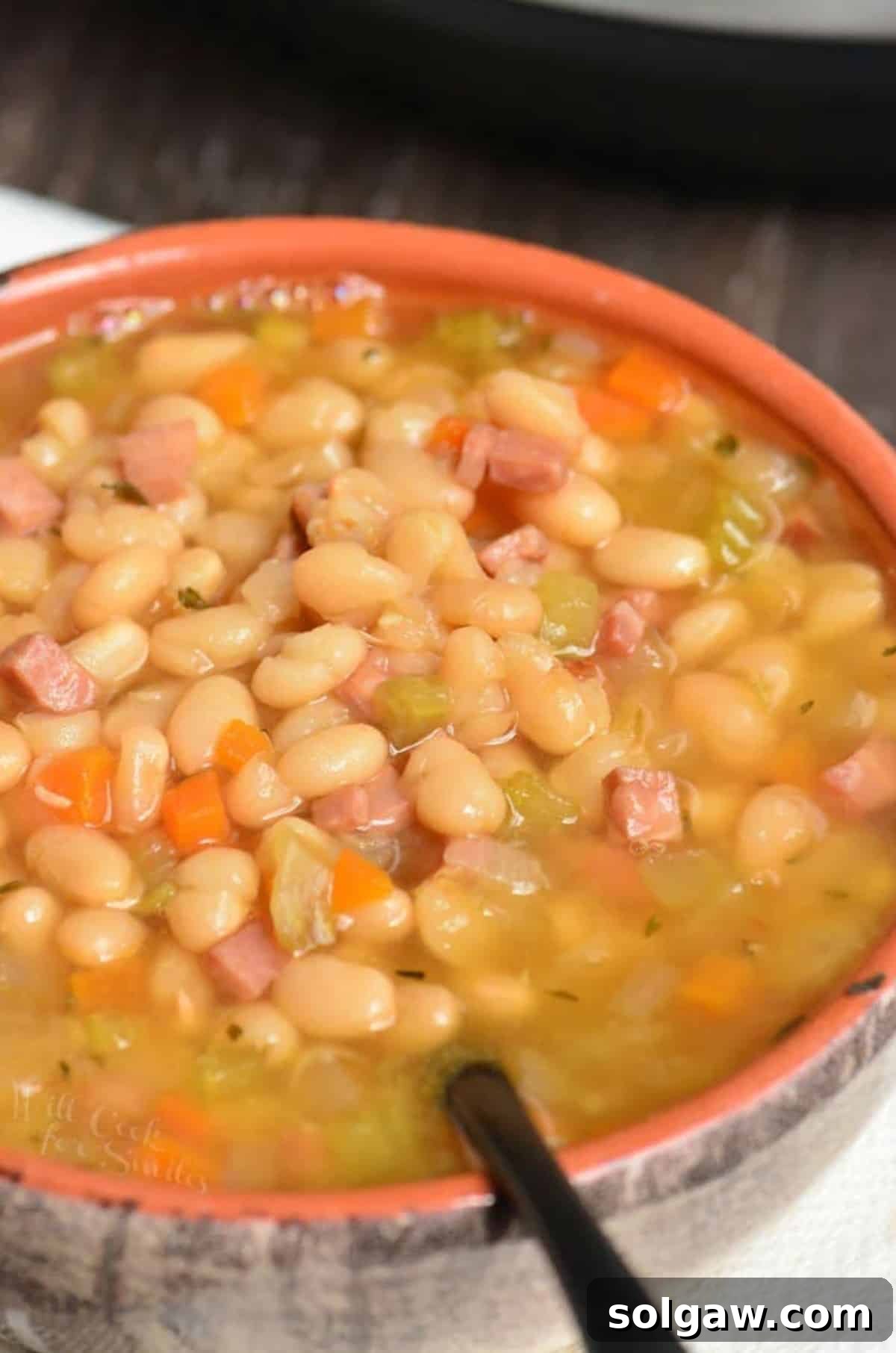 A steaming bowl of Instant Pot Ham and Bean Soup, with a spoon gently scooping out a portion, highlighting its rich texture and ingredients.