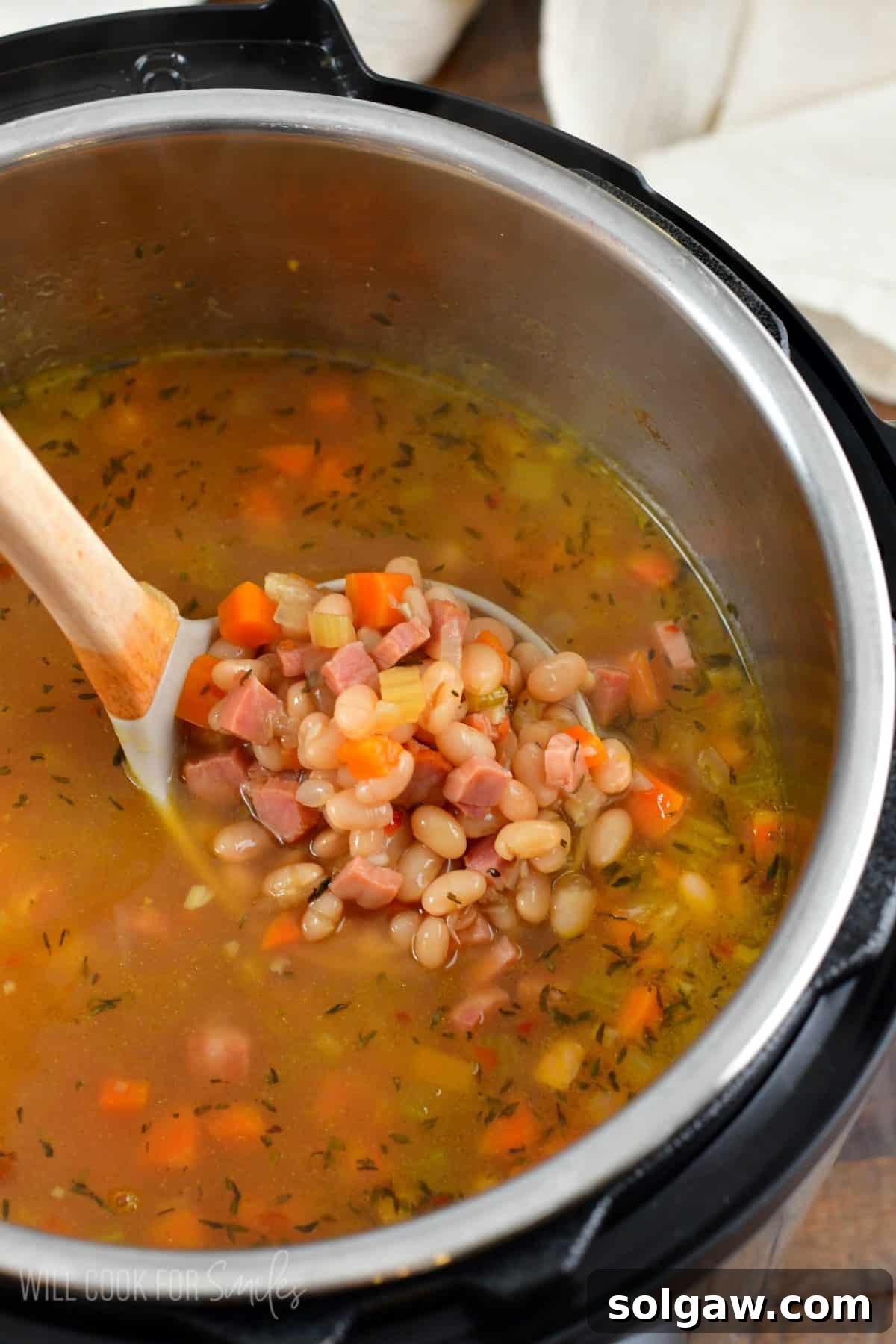 A close-up shot of rich ham and bean soup in an Instant Pot, with a wooden ladle lifting a spoonful, highlighting its thick texture and wholesome ingredients.