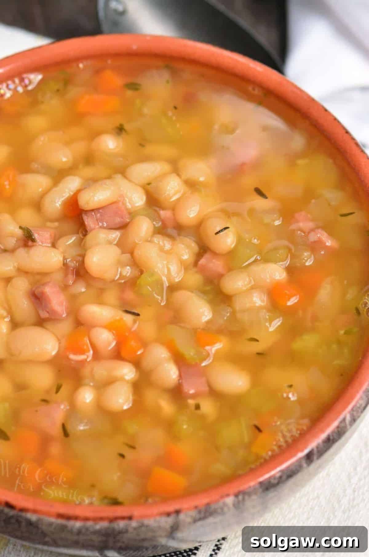 A close-up of a bowl filled with steaming ham and bean soup, garnished with fresh herbs, ready to be enjoyed.