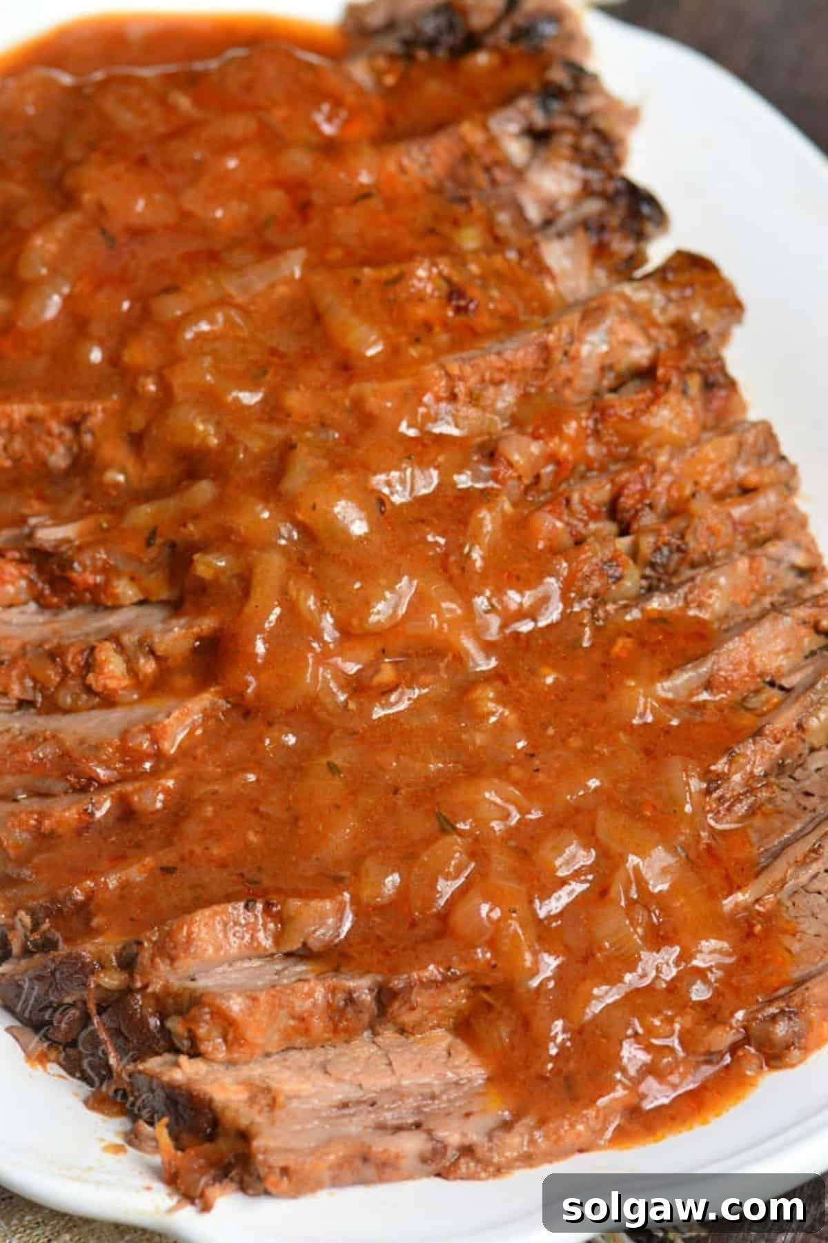 juicy and tender fall apart beef brisket sliced and topped with French onion sauce on a white plate.